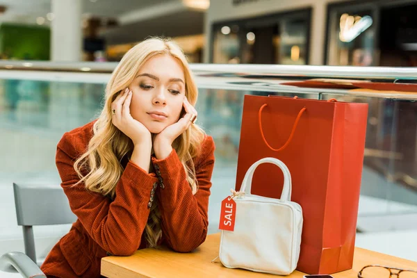 Mulher chateada sentado no shopping com um saco de compras e um saco com etiqueta de venda — Fotografia de Stock