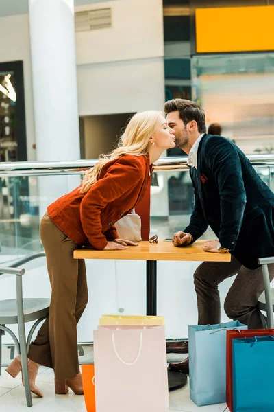 Stylish couple of shopaholics kissing in cafe in shopping center — Stock Photo