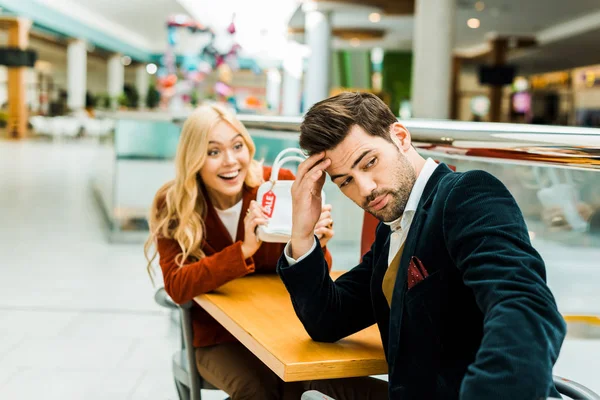 Excited woman showing bag with sale tag to frustrated man — Stock Photo