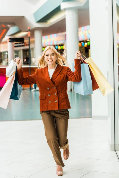 Bela mulher animada com sacos de compras em execução no shopping — Fotografia de Stock