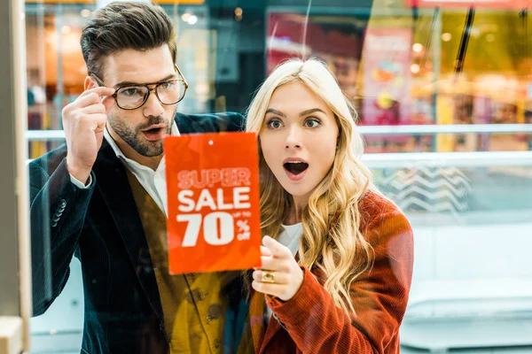 Beautiful excited couple of shopaholics looking at super sale with 70 percents discount in shopping center — Stock Photo