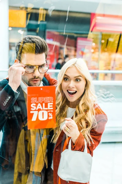 Beautiful shocked couple of shopaholics looking at super sale with 70 percents discount in shopping center — Stock Photo