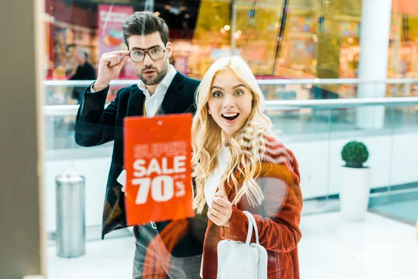 Surprised couple looking at super sale with 70 percents discount in shopping center — Stock Photo