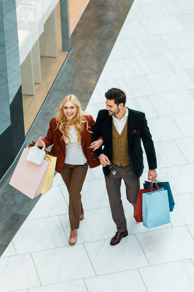 Vista aérea de pareja feliz con bolsas de compras caminando en el centro comercial - foto de stock