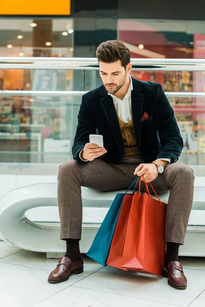 Schöner Mann mit Smartphone in Einkaufszentrum mit Taschen — Stockfoto