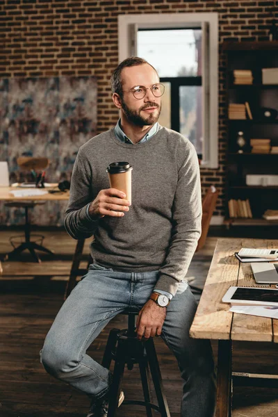 Homem de negócios casual sentado na mesa e segurando xícara de café no escritório loft — Fotografia de Stock