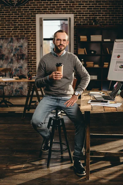 Homem de negócios casual sentado na mesa e segurando xícara de café no escritório loft — Fotografia de Stock