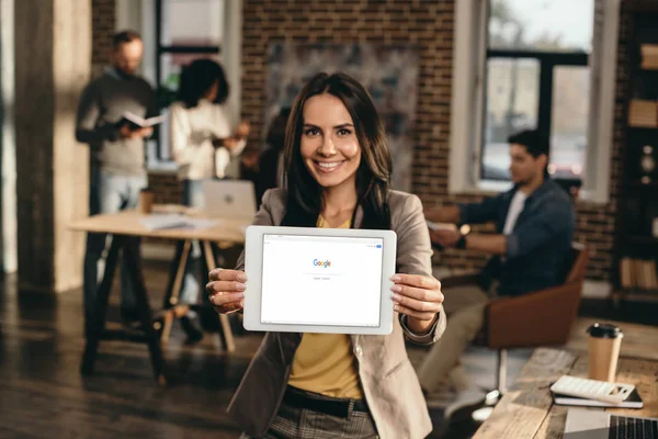 Glückliche Gelegenheitsunternehmerin hält Tablet mit Google-Website auf dem Bildschirm im Loft-Büro mit Kollegen, die dahinter arbeiten — Stockfoto