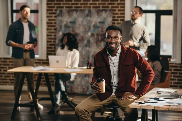 African american casual businessman drinking coffee with colleagues working behind in loft office — Stock Photo