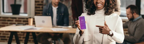 Щасливі афро-американських випадковий бізнес-леді вказуючи на смартфон з instagram app в лофт офісу з колегами за — стокове фото