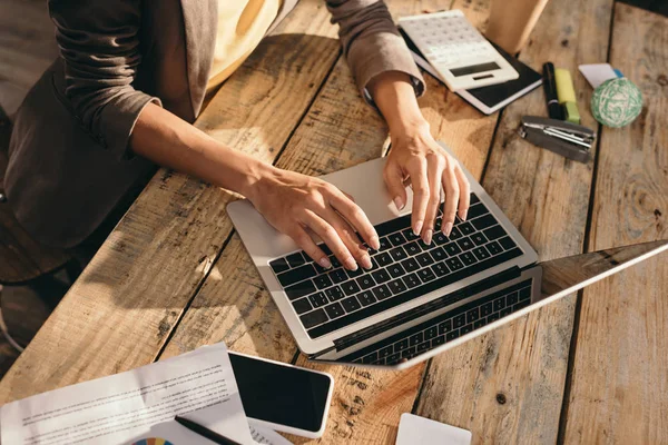 Vue recadrée des mains féminines tapant sur ordinateur portable au bureau avec fournitures de bureau — Photo de stock