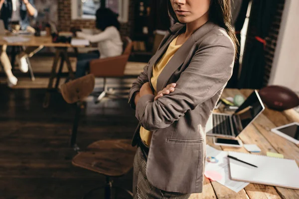 Vista recortada de la mujer de negocios de pie en el escritorio en la oficina loft con colegas de fondo — Stock Photo