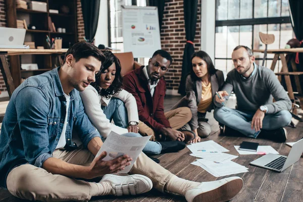 Serio gruppo multietnico di colworkers seduti sul pavimento e discutere insieme nuovo progetto in ufficio loft moderno — Foto stock