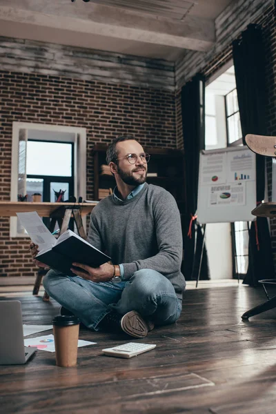 Homme d'affaires occasionnel assis sur le sol avec ordinateur et travaillant sur le projet dans le bureau loft moderne — Photo de stock