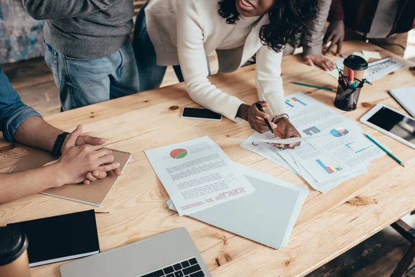 Cropped view of multiethnic group of colleagues at desk working together on new project in loft office — Stock Photo