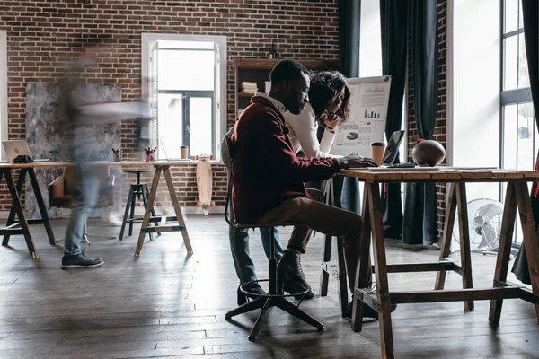 Couple afro-américain d'hommes d'affaires occasionnels travaillant au bureau avec des collègues en mouvement flou dans le bureau loft moderne — Photo de stock