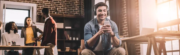 Casual businessman using smartphone with multiethnic group of working colleagues behind in modern loft office — Stock Photo