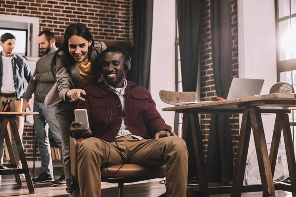 Pareja de compañeros de trabajo tomando selfie usando smartphone con dos colegas en segundo plano - foto de stock