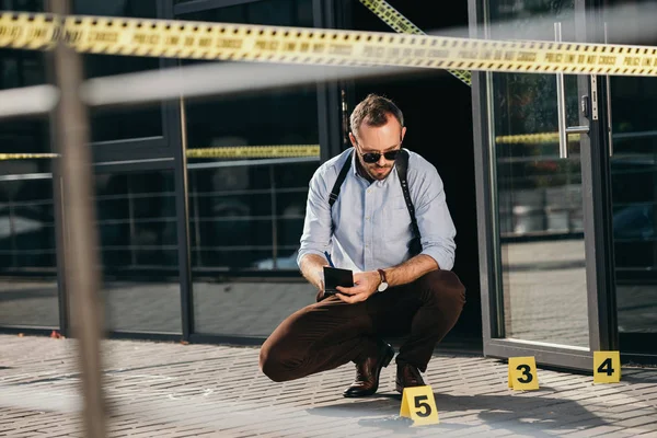 Sitzender männlicher Detektiv, der sich den Hinweis ansieht und Notizen macht — Stockfoto