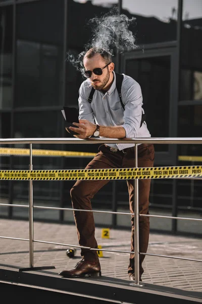 Detective masculino fumando y mirando notas apoyadas en la valla - foto de stock