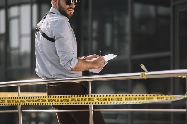 Détective masculin dans des lunettes de soleil prendre des notes — Photo de stock