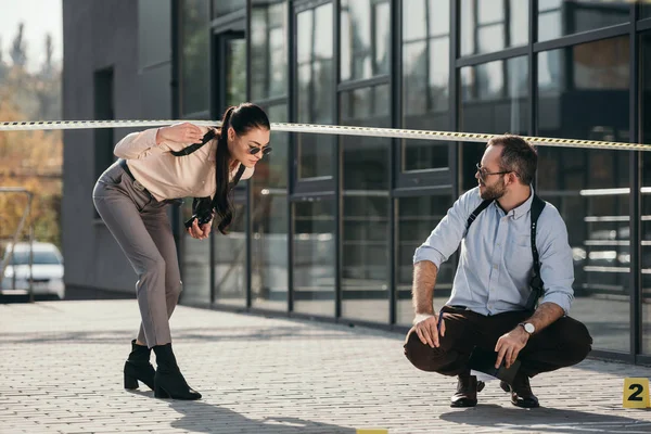 Detective hombre esperando a detective mujer que cruza la línea de policía - foto de stock