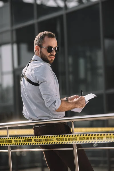 Вид збоку чоловічий детектив в сонцезахисних окулярах робить нотатки — стокове фото