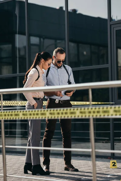 Male and female detectives standing at crime scene and looking at notebook — Stock Photo