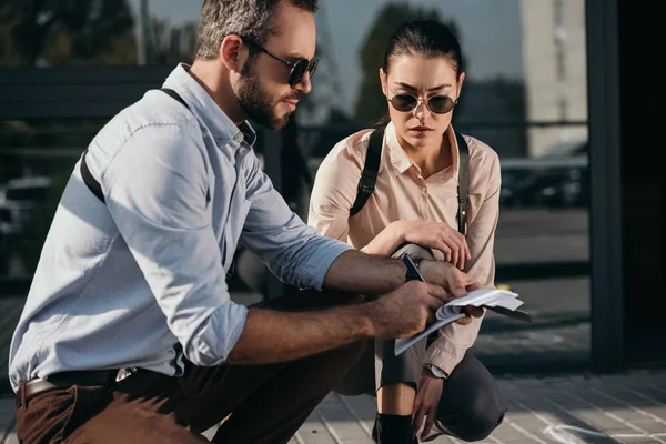 Detectives masculinos y femeninos sentados y leyendo sus notas - foto de stock