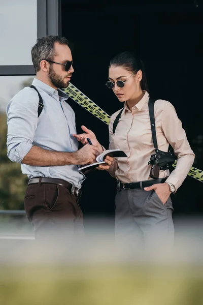 Partial view of female and male detectives in sunglasses review their records at crime scene — Stock Photo