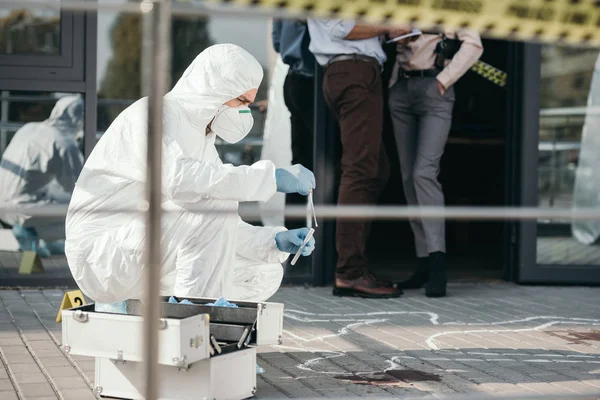 Criminólogo masculino en traje de protección y guantes de látex recogiendo pruebas en la escena del crimen - foto de stock