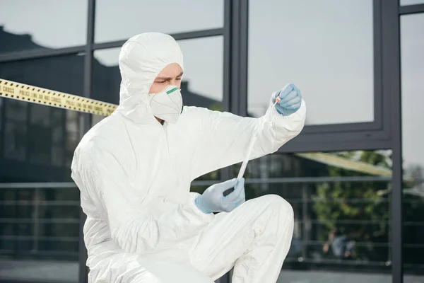 Criminólogo masculino en traje de protección y guantes de látex mirando las pruebas en la escena del crimen - foto de stock