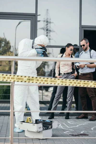 Criminólogo haciendo foto de la escena del crimen en cámara con dos detectives detrás de él - foto de stock