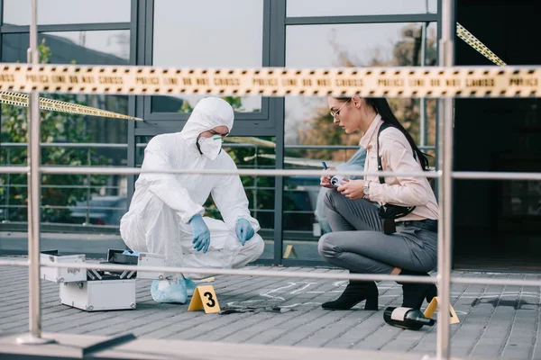 Detective feamale y criminólogo masculino inspeccionando la escena del crimen - foto de stock