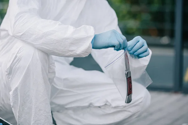 Cropped view of criminologist in protective suit and latex gloves taking evidence into flask at crime scene — Stock Photo