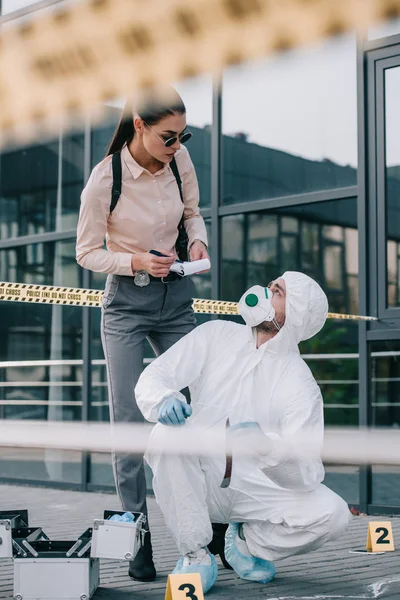 Detective mujer escribiendo explicación al criminólogo en la escena del crimen - foto de stock