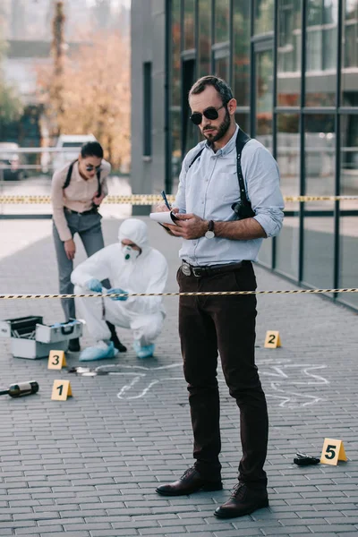 Male detective standing at crime scene and making some notes — Stock Photo