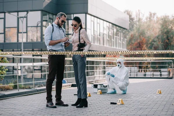 Female and male detectives review their records at crime scene — Stock Photo