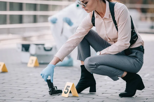 Femme détective prenant arme comme indice avec criminologue derrière sur la scène de crime — Photo de stock