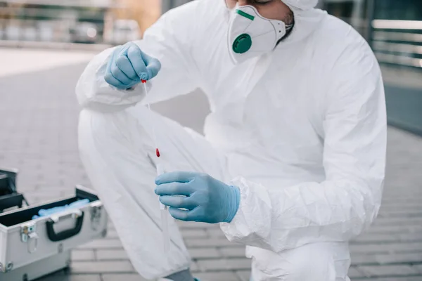 Cropped view of male criminologist in protective suit and latex gloves putting evidence into test tube at crime scene — Stock Photo