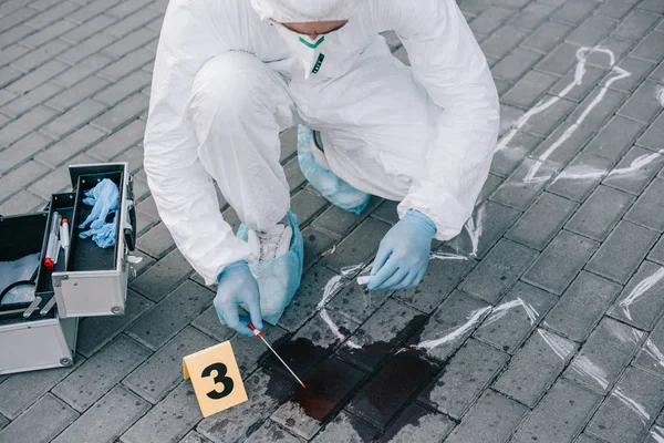 Criminologue masculin en combinaison de protection et gants en latex prélevant un échantillon de sang sur les lieux du crime — Photo de stock