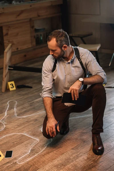 Serious male detective sitting at crime scene and looking on chalk line — Stock Photo