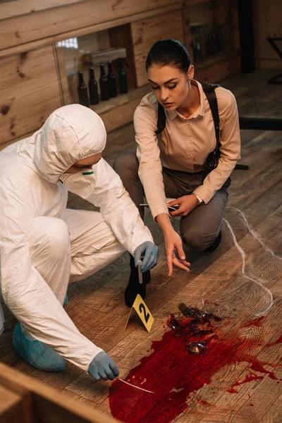 Angle view of forensic investigator and serious female detective taking samples and examining crime scene — Stock Photo