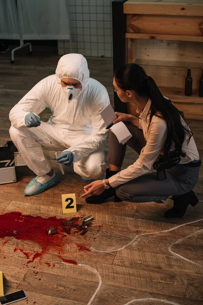 Forensic investigator and concentarted female detective taking notes and investigating crime scene together — Stock Photo