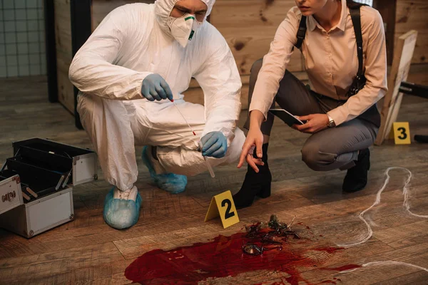 Cropped view of forensic investigator and female detective taking notes and examining crime scene — Stock Photo