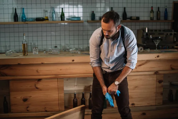 Detective masculino serio que usa guantes de látex para examinar la escena del crimen - foto de stock