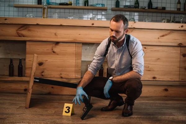 Detective masculino serio recogiendo evidencia arma en la escena del crimen - foto de stock