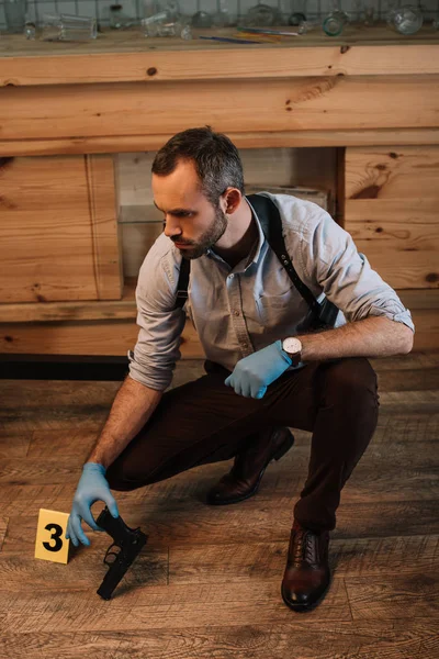 Detective masculino concentrado recogiendo evidencia arma en la escena del crimen - foto de stock