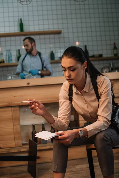 Détective féminine fumeuse sérieuse assise sur la scène de crime avec un collègue travaillant derrière — Photo de stock