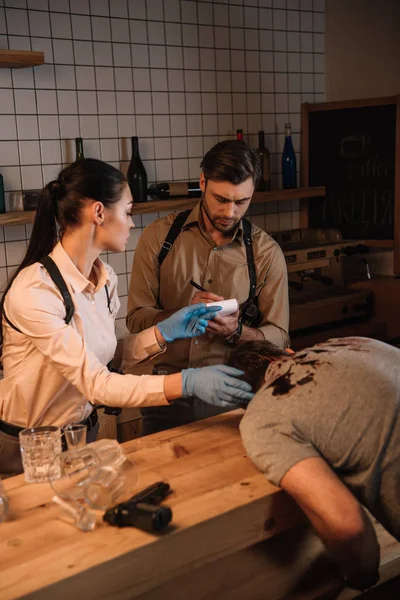 Concentated female and male detectives collecting evidence from dead body and investigating crime scene — Stock Photo